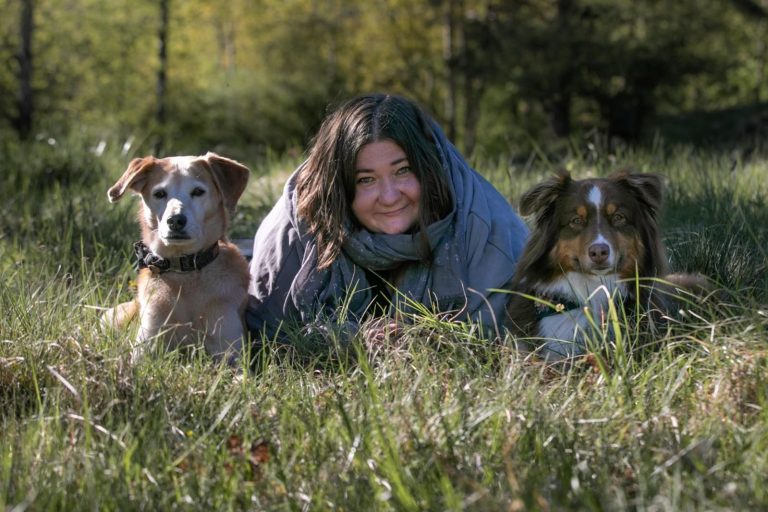 Eine Person liegt auf einem Holzweg und wird von zwei Hunden umgeben.