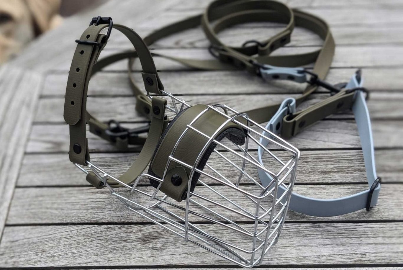 Biothane in der Maulkorb Anpassung Hundemaulkorb aus Metall mit passenden Gurten auf einem Holztisch ausgebreitet.